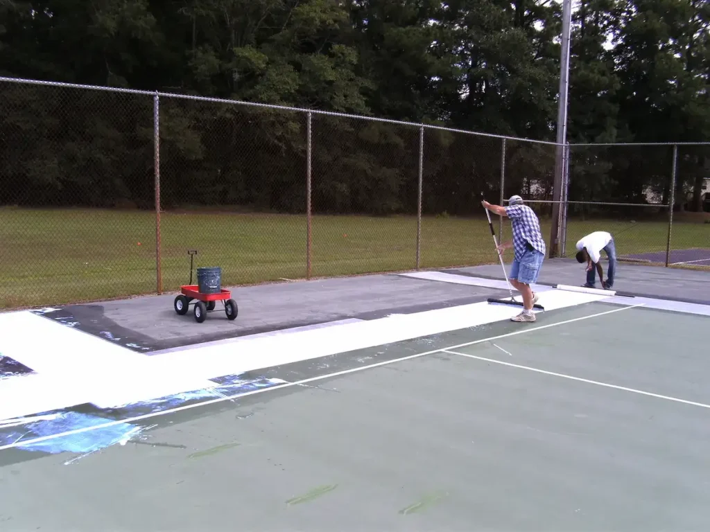 crew applying resurfacing materials during outdoor tennis court resurfacing project